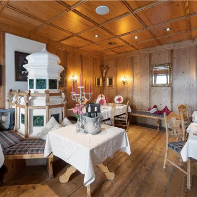 A cozy restaurant with wooden walls and elegantly set tables. In the center stands a traditional tiled stove.
