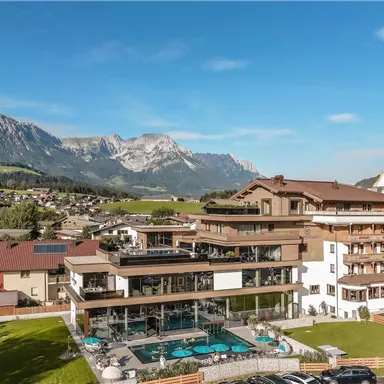 A modern hotel with a swimming pool and a beautiful view of the mountains. The surroundings are green and idyllic, perfect for a relaxing vacation.