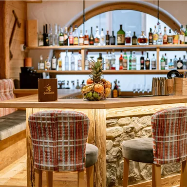A cozy bar with wooden details and an inviting seating area. In the background, shelves decorated with various drinks are visible.
