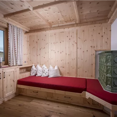 Ein gemütlicher Raum mit Holzverkleidung und einem roten Sofa. Durch das Fenster ist ein Ausblick auf die Natur zu sehen.