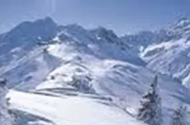 A snow-covered mountain landscape under a clear blue sky. The sun shines brightly, giving the scene a sparkling glow.