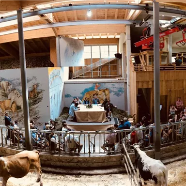 A large barn with cows and people. A mural is visible in the background.