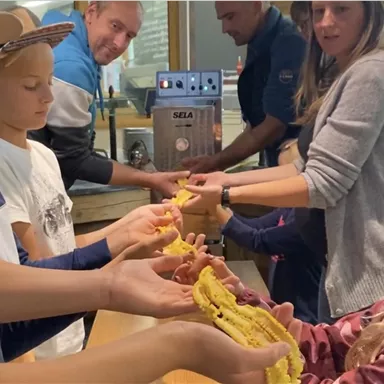 A group of children and adults stands together, holding colorful, twisted craft materials in their hands. They appear focused and enjoy the shared activity.