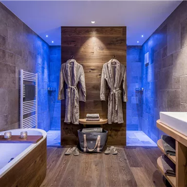 A modern bathroom with a bathtub, wooden details, and elegant lighting. Two bathrobes hang on the wall, and the space feels relaxing and inviting.