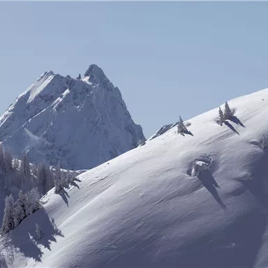 A snow-covered mountain landscape with a high peak in the background. The sky is clear and blue, creating a tranquil atmosphere.