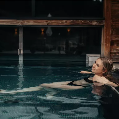Eine Frau entspannt im Wasser eines Wellnesspools. Der Raum ist modern und gemütlich gestaltet.