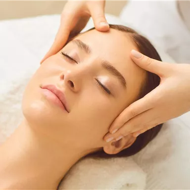 A woman is receiving a relaxing facial treatment. Gentle hands are massaging her face in a calm environment.