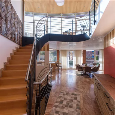 A modern and stylish living room with an open wooden staircase. Large windows allow plenty of light in and create an inviting atmosphere.