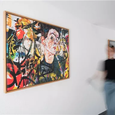 A lively artwork on a wall with vibrant colors and dynamic patterns. A person walks past the painting, creating a connection between art and movement.