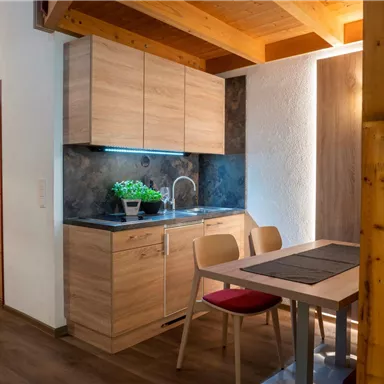 A modern kitchen with wooden cabinets and a small dining area. The space has a bright, inviting atmosphere.