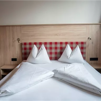 A cozy bedroom with a double bed and wooden paneling. The pillows are stylishly arranged, and the walls have a bright, friendly color scheme.