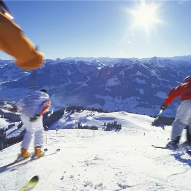 Skiers descend a snowy slope. The sunny sky and the impressive mountains in the background create a perfect winter landscape.