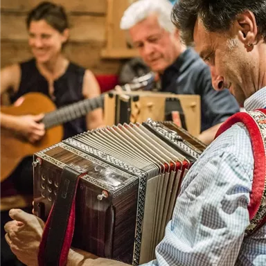 A musical performance in a cozy environment. A man plays the accordion while other musicians join in with guitars.