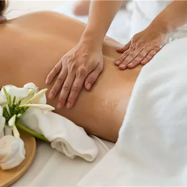 A relaxing massage is performed on a person's back. Oils and fresh flowers are lying next to the massage table.