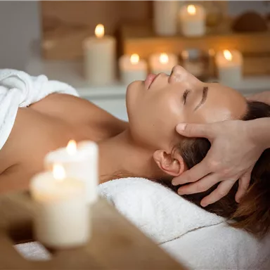 A relaxing spa scene with a woman receiving a head massage. Candlelight creates a calm atmosphere in the background.