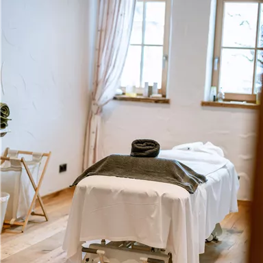 A relaxing massage room with a treatment table and natural light. The walls are light and the decor feels cozy.