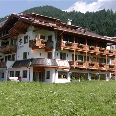 A charming building in alpine style with several balconies. Surrounded by green meadows and mountains in the background.