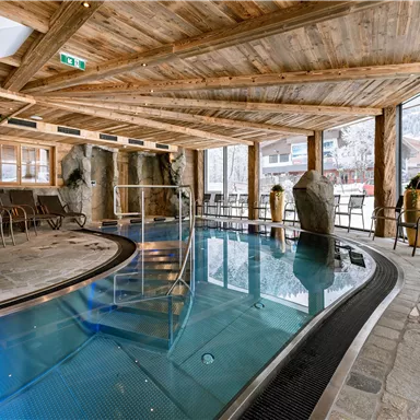 An elegant indoor pool in a wooden-decorated room. The light gently falls through the windows, creating a relaxing atmosphere.
