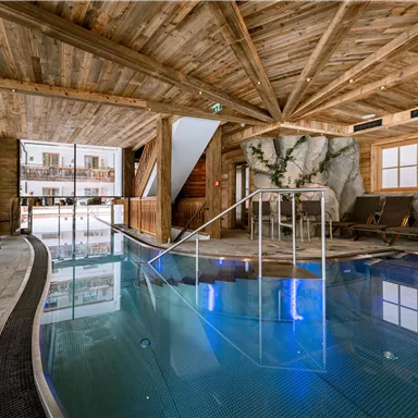 An elegant indoor pool in a wooden décor room. The atmosphere is relaxing with comfortable loungers and large windows.
