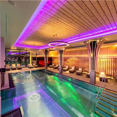 A modern spa area with a pool illuminated by colorful LED lights. Cozy loungers surround the pool, creating a relaxed atmosphere.