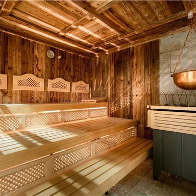 A quiet sauna with a wooden bench and warm light. The walls are clad in wood and a copper bowl hangs from the ceiling.
