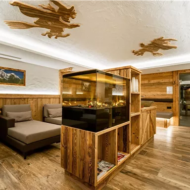 A cozy room with wooden furniture and a central aquarium. Ceiling decorations and warm lighting create an inviting atmosphere.