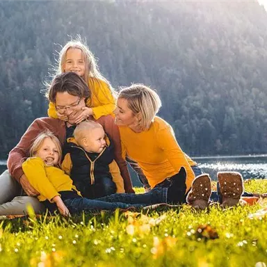 A family is sitting on a meadow by the shore of a lake. They are wearing cheerful yellow clothing and enjoying a sunny day in nature.