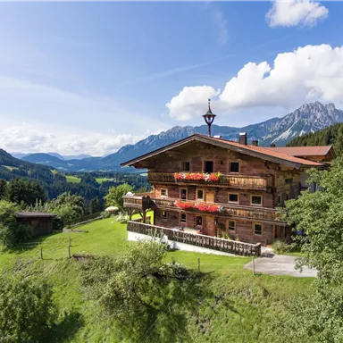 A charming wooden house in the mountains with beautiful flower balconies. The surroundings are green and picturesque with majestic mountains in the background.