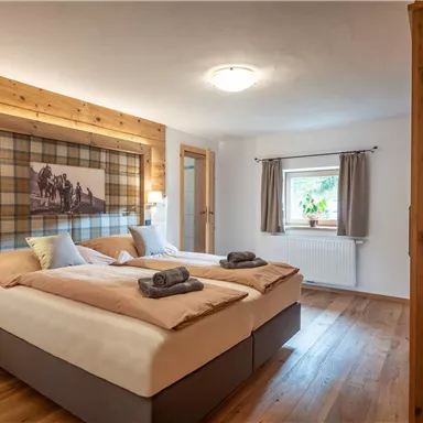 A modernly furnished room with two beds and wooden details. There is a cozy atmosphere with a window and a television on the wall.