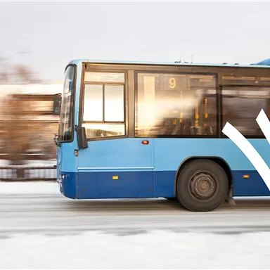 Ein blauer Bus fährt schnell auf einer schneebedeckten Straße. Im Hintergrund sind unscharfe Bäume sichtbar.