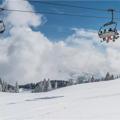 Eine verschneite Landschaft mit einem Skilift und Wolken im Hintergrund. Die Bäume sind mit Schnee bedeckt und es herrscht eine klare, kalte Atmosphäre.