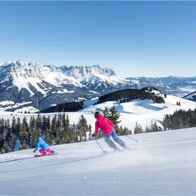 Ein wunderschönes Winterland mit schneebedeckten Bergen. Zwei Skifahrer fahren über die präparierte Piste.