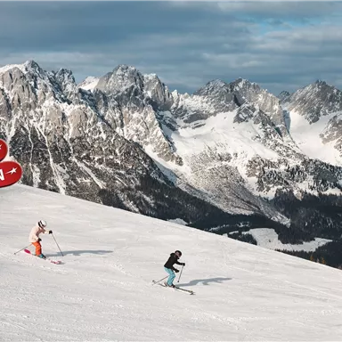Two skiers are skiing down the snow-covered slope in the mountains. In the background, majestic mountain peaks can be seen.