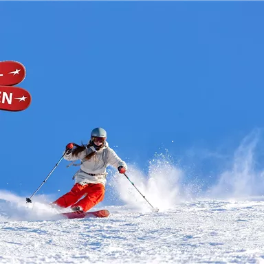 A skier glides over fresh snow under a clear blue sky. In the background, signs reading "SUPER SKI WEEKS" can be seen.