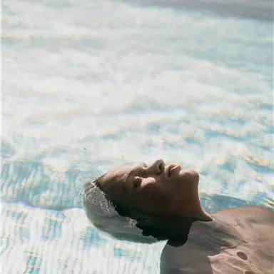 Ein Mann liegt entspannt auf dem Wasser in einem Pool. Die sanften Wellen spiegeln das Licht wider und schaffen eine ruhige Atmosphäre.