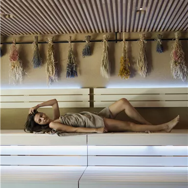 A woman is lying relaxed on a modern lounge chair. In the background, decorative elements hang on the wall.