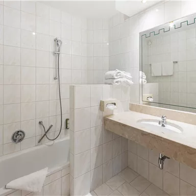 A modern bathroom with a bathtub and shower. The walls are tiled in light colors and there is a large mirror above the sink.