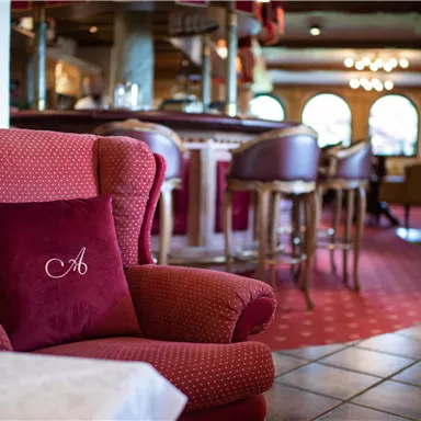 A cozy armchair with a red cushion is in a stylish interior. In the background, there are a bar and elegant chairs.