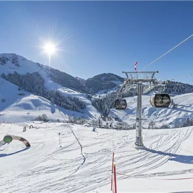 Eine malerische Winterlandschaft mit schneebedeckten Bergen und einem Sessellift. Der klare Himmel und die Sonne strahlen in der frischen, kalten Luft.