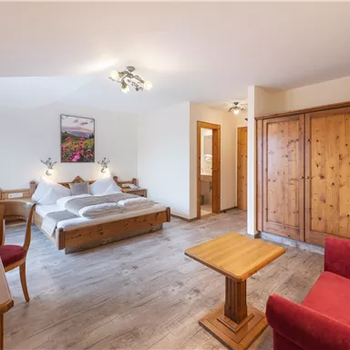 A cozy bedroom with a double bed and a red sofa. Wooden furniture and a TV complete the inviting atmosphere.