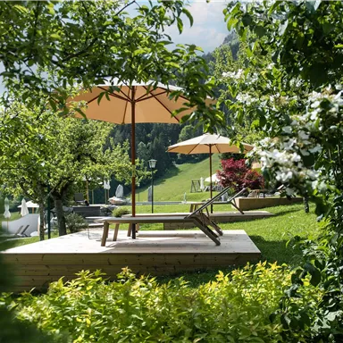 A peaceful garden with lounge chairs and sun umbrellas. Surrounded by lush greenery and blooming plants.