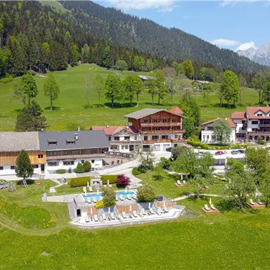 A picturesque hotel in the greenery, surrounded by mountains and meadows. The outdoor area features a pool and well-maintained gardens.