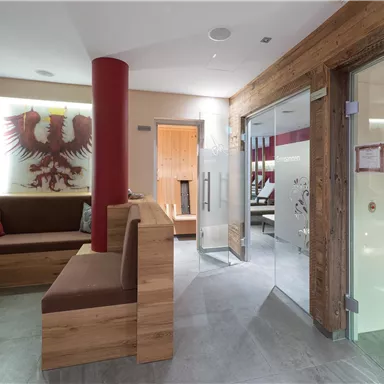 A modern wellness area with wood and stone elements. On the left side, there are comfortable seating areas and a glass door leads to another room.
