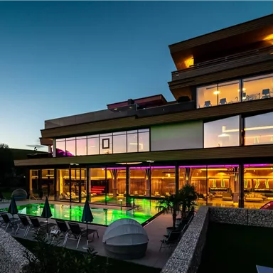 A modern building with large windows and a lit pool. The surroundings are quiet and surrounded by mountains.