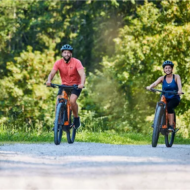 Two cyclists on a gravel path in a green environment. Both are wearing helmets and enjoying nature.