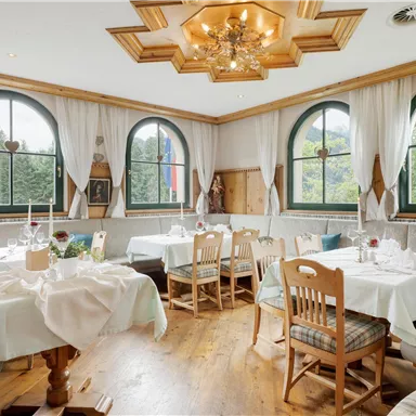 A cozy restaurant with wooden furniture and large windows. The tables are decorated with white tablecloths and flowers.