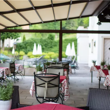An inviting restaurant with covered tables and red tablecloths. In the background, well-maintained green areas and loungers can be seen.