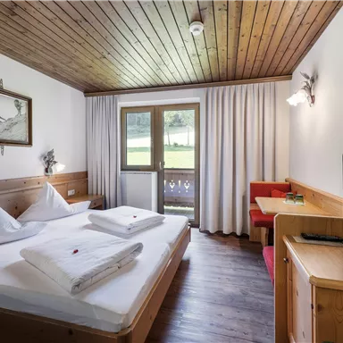 A cozy room with a double bed and wooden paneling. There is a balcony, a television, and a seating area.