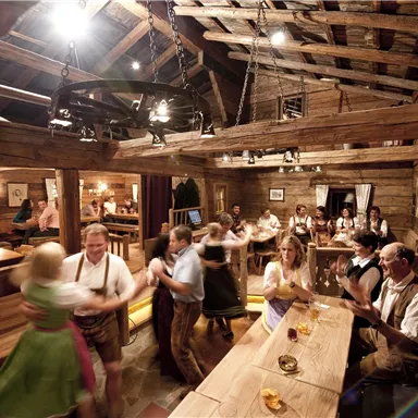 A cozy alpine inn with wooden interiors. People in traditional clothing are dancing and celebrating.