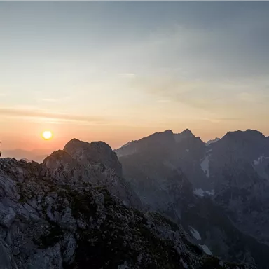 Two hikers stand on a mountain peak at sunset. The view of the surrounding mountains is impressive and majestic.